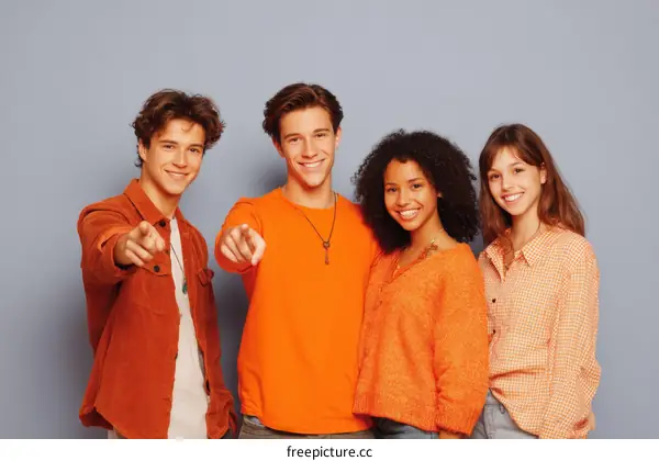 Group of young friends pointing fingers at camera against gray background