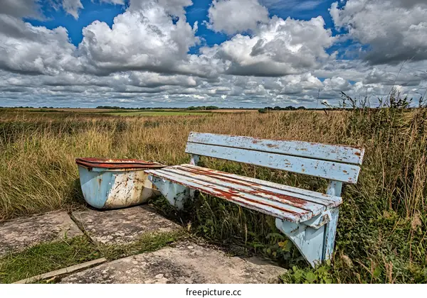 Rustic Bench Under a Cloudy Sky with Green Fields in the Background