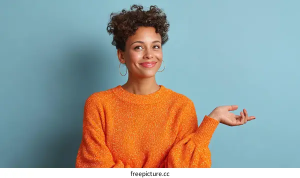 Smiling woman in orange sweater gesturing with hand against blue background