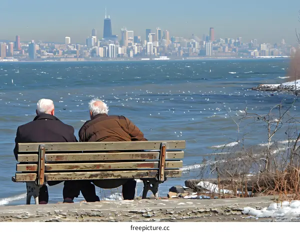 Two Senior Men Sit On Bench Overlooking City Skyline