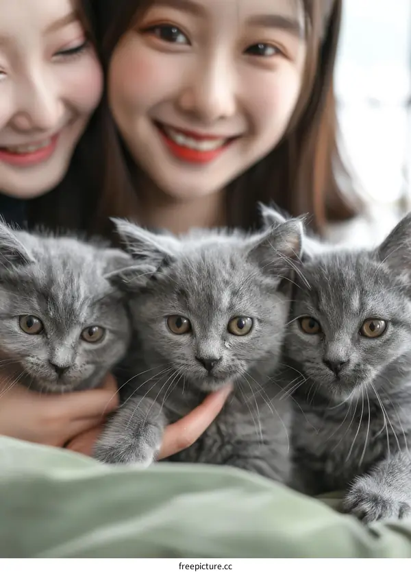 Two young Asian women with three gray kittens