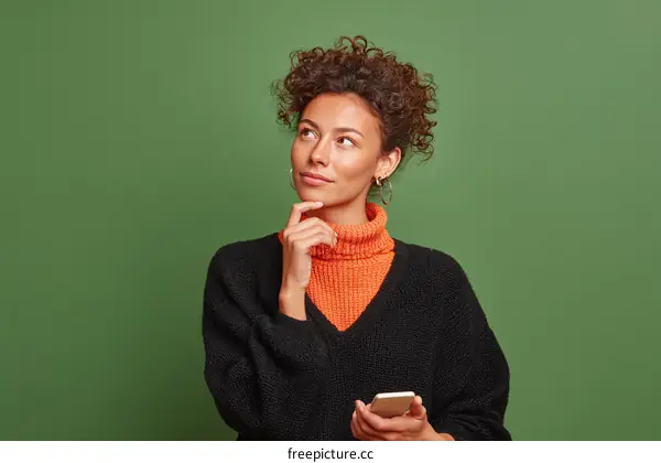 Thoughtful Woman Holding a Mobile Phone Against Green Background
