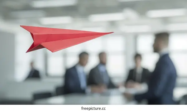 Red paper plane flying in an office with people in the background