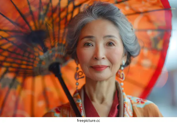 Portrait of a smiling elderly Asian woman holding a red umbrella