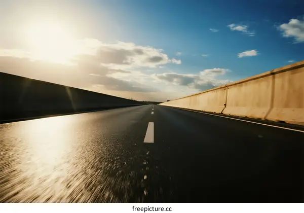 Sunlit highway with clear blue sky and clouds in the distance