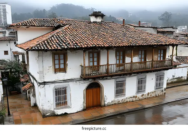 White Colonial Style House with Red Tile Roof and Wooden Balcony in a Mountain Town