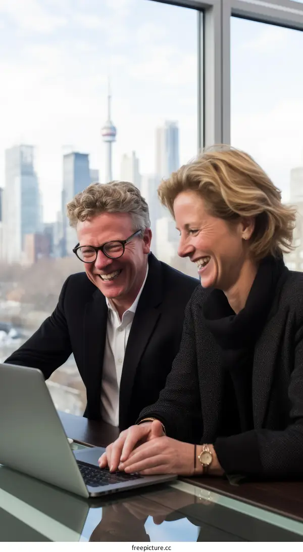 Blond man and woman in dark suit looking at laptop and laughing
