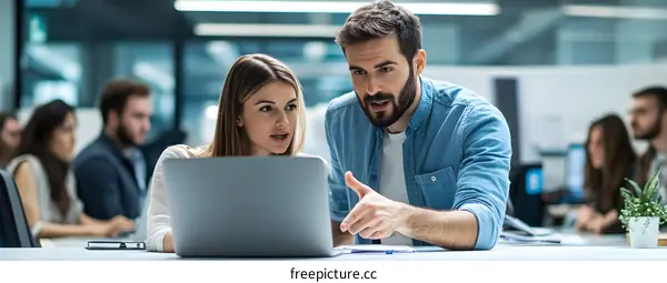 Two Colleagues Discussing Work On Laptop in Office