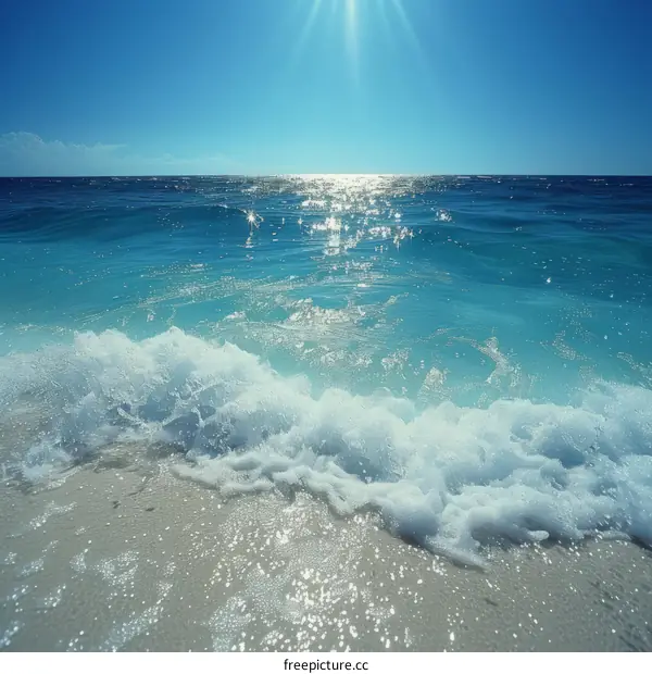 The sun shines on the blue sea and white waves gently lap the sandy shore