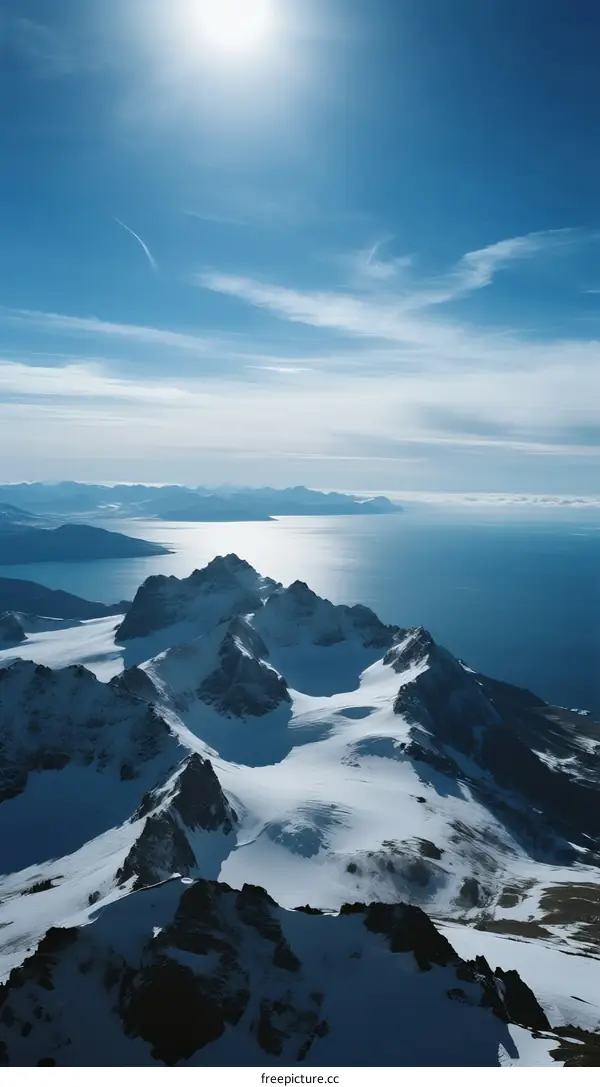 Snow-covered mountain peaks with blue sky and sea in background