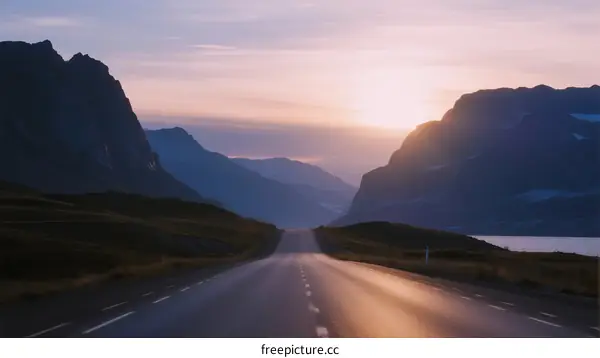 Sunlit road stretching through majestic mountain ranges at dawn