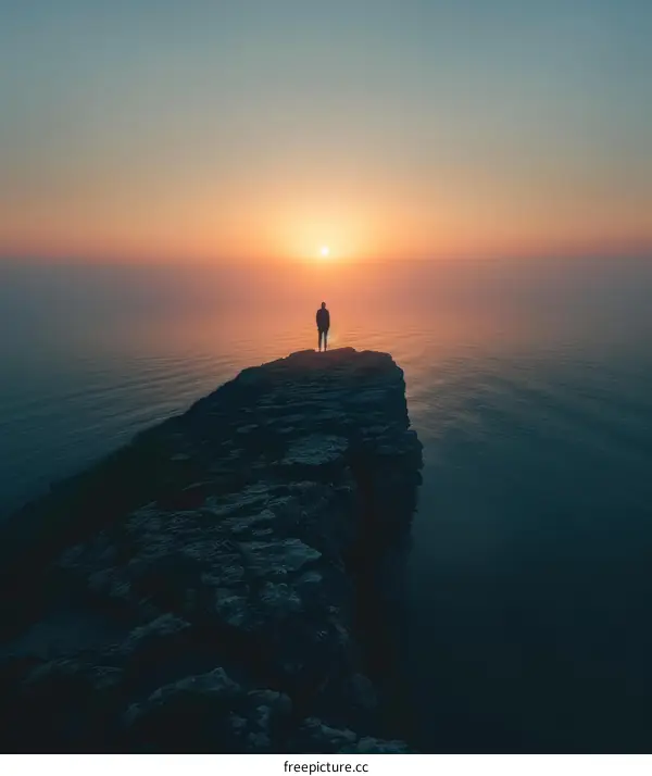 Man standing alone on a cliff overlooking a vast body of water during sunset