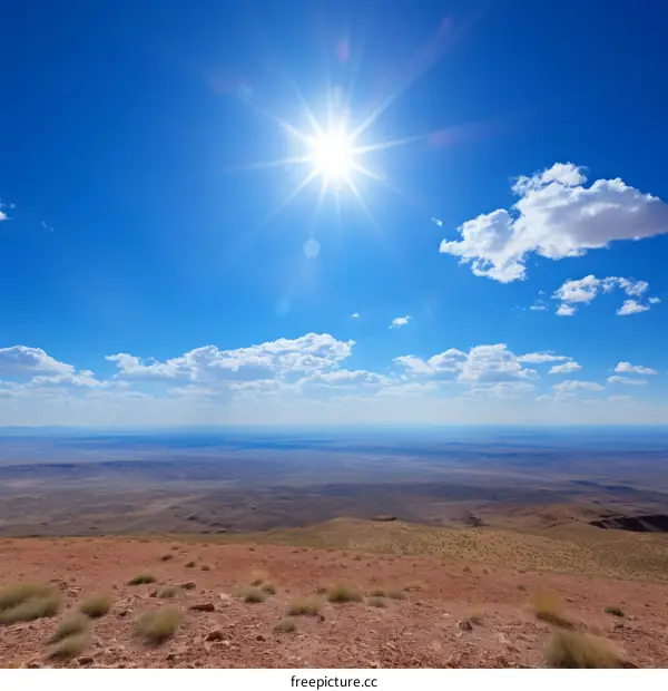 A vast desert landscape with a bright sun and a few clouds in the sky