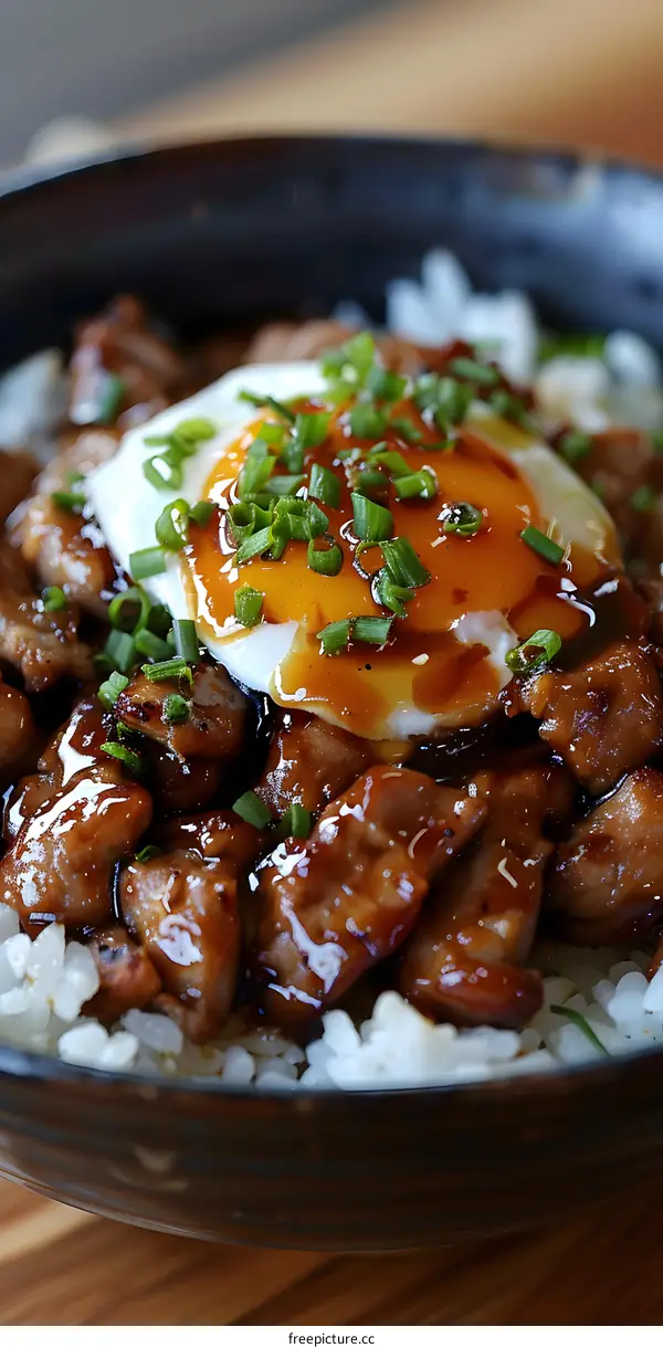A bowl of Japanese chicken teriyaki donburi topped with a raw egg and spring onions
