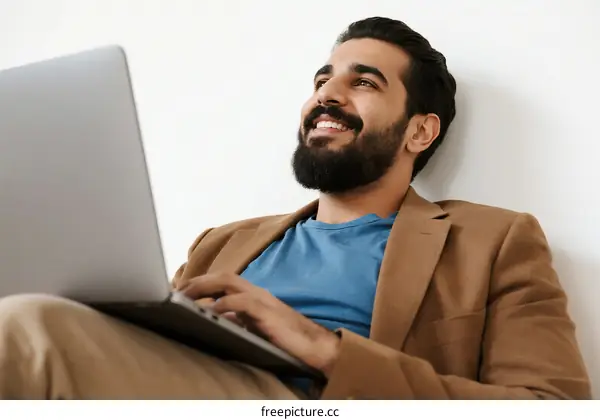 A man sitting comfortably using a laptop with a relaxed expression