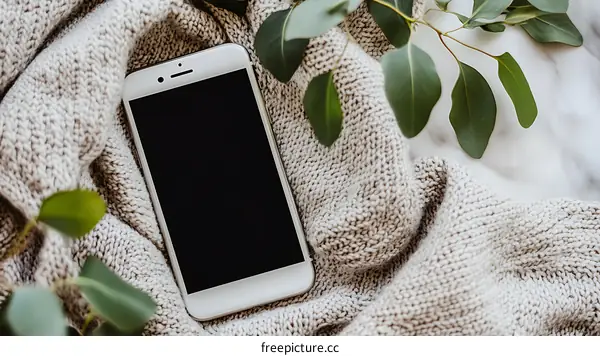 White Smartphone On Knitted Blanket With Green Leaves