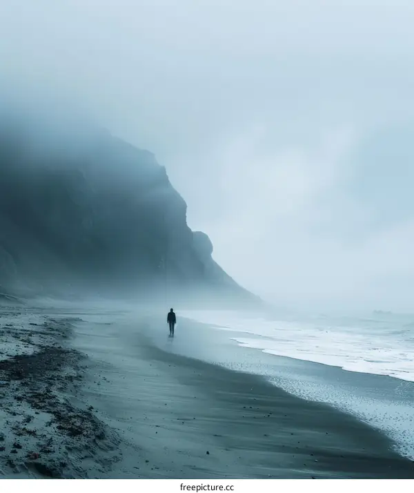 Man walking alone on a beach with a large rock formation in the background