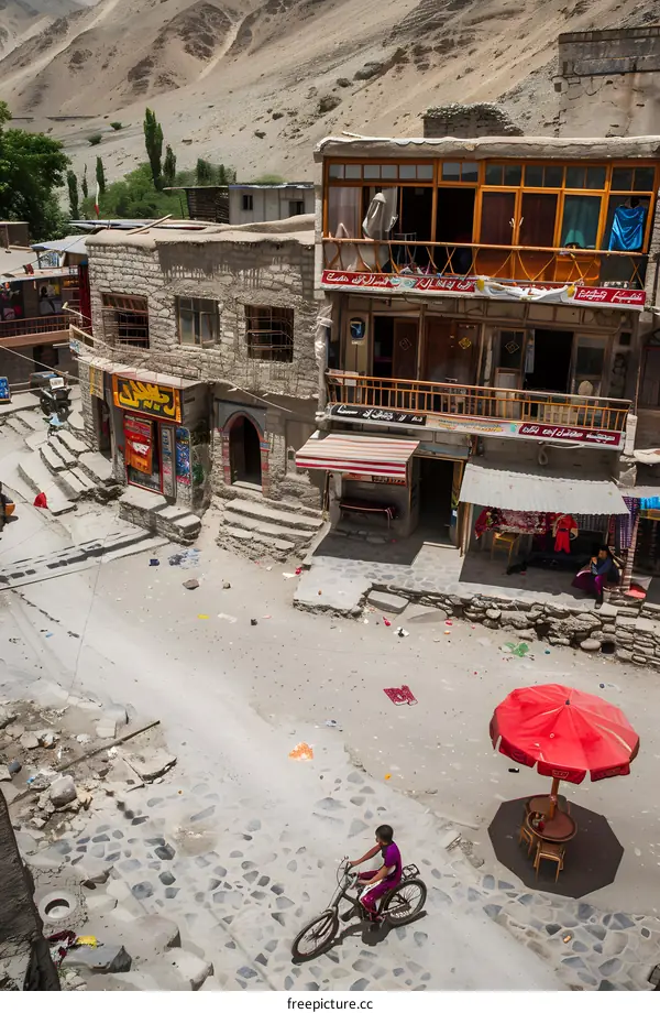 Mountain Village Street Scene with Cyclist and Red Umbrella