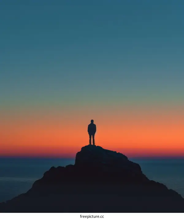Man standing alone on a rock in front of the ocean at sunset
