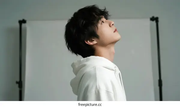 Young man in white hoodie looking up against white background