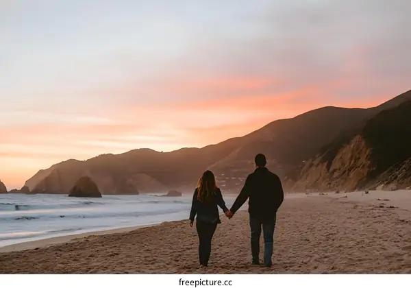 Couple Holding Hands Walking On Beach At Sunset