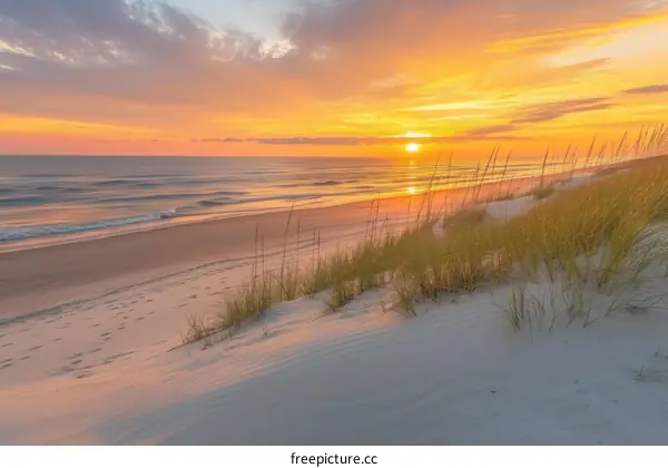 beach sunset over calm sea with footprints in sand dunes
