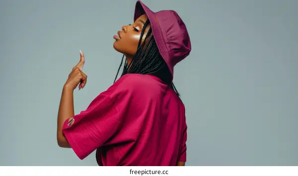 A young woman wearing a bucket hat and a pink t-shirt is pointing her finger at something.