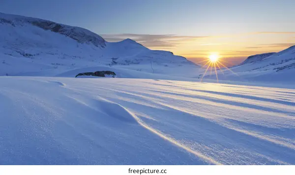 A beautiful winter landscape with a snow covered mountain and a setting sun