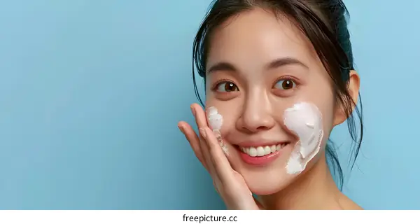 Beautiful Asian Woman Applying Facial Cream on Blue Background