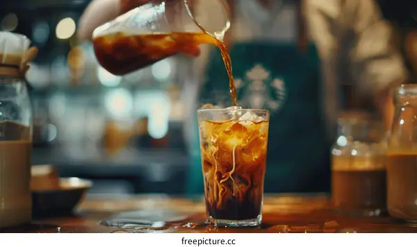 Barista pouring milk into glass of iced coffee