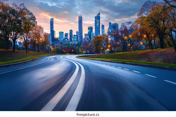 Cityscape image of a road with autumn trees and a modern downtown skyline in the background