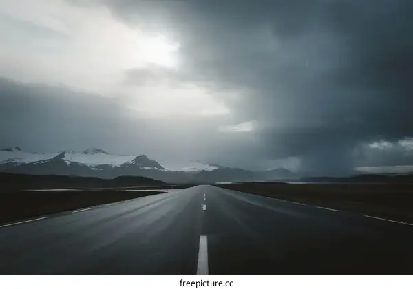 Long Road Under Dark Stormy Clouds with Snowy Mountains in the Distance
