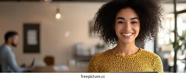 Smiling African American Woman in a Yellow Blouse Holding a Tablet in a Modern Office
