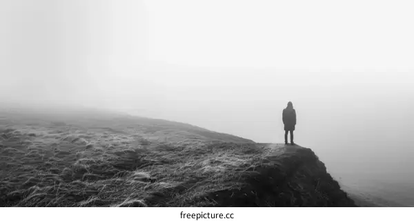 Person standing alone on a cliff edge looking out at a foggy landscape