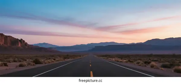 Long straight road stretching through a desert landscape at sunset