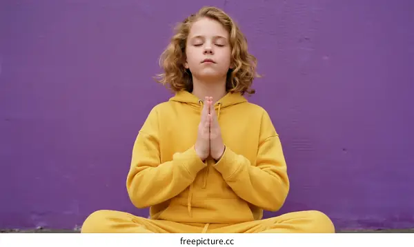 A Young Girl in Yellow Hoodie Meditating in Front of Purple Wall