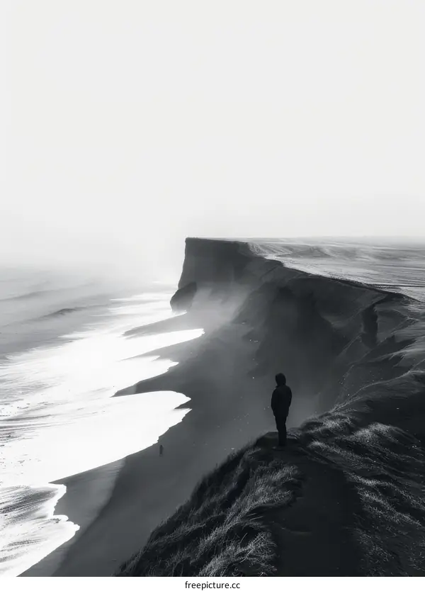 Black and white photo of a person standing on a cliff overlooking the ocean