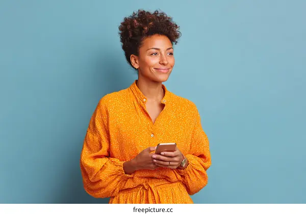 Smiling young woman wearing orange dress holding smartphone