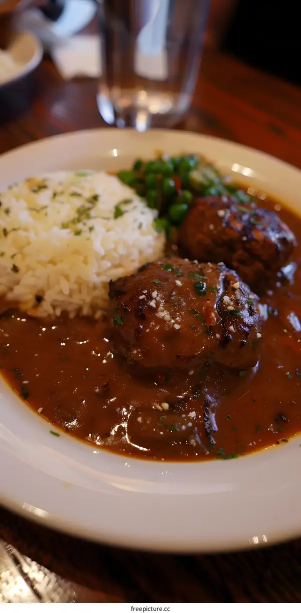 A plate of Salisbury steak with rice and peas