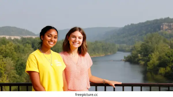 Two Young Women Smiling at Scenic River View