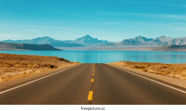 Endless road leading to clear blue lake with mountains in background