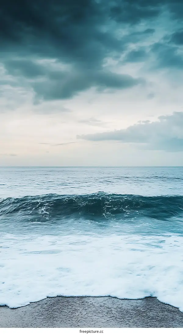 Ocean Waves Crashing on Sandy Beach Under Cloudy Sky
