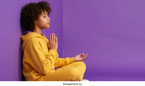 Young Girl in Yellow Tracksuit Meditating Against Purple Wall
