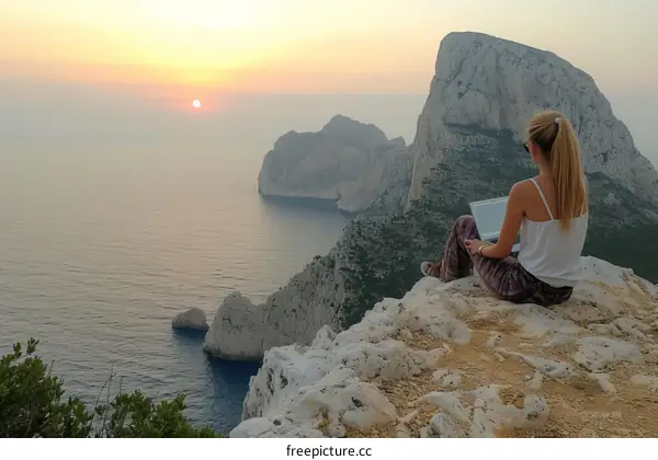 Young woman sitting on a cliff and using laptop