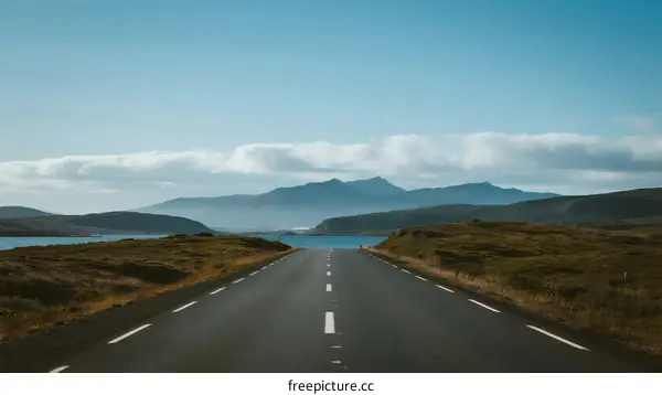 A long empty road stretching towards distant mountains and a lake