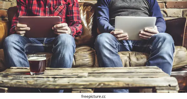 Two Men Sitting On A Couch With Tablets