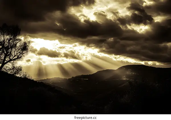 Sun Rays Shining Through Dark Clouds Over Mountains