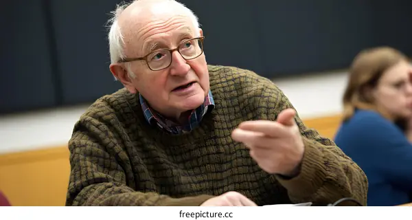 Senior Man Wearing Glasses and a Sweater Speaking in a Classroom