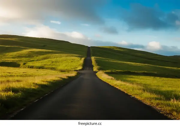 A Long Road Stretching Through Green Rolling Hills Under a Blue Sky