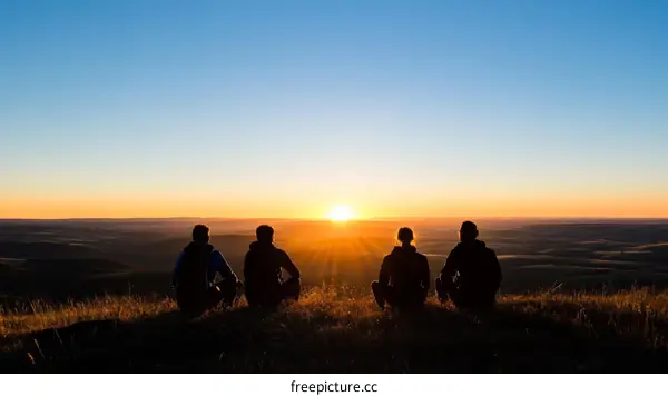 Silhouette of Four People Watching Sunrise over Landscape